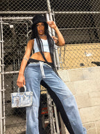 Woman in casual outfit with denim jeans and crop top, standing against a chain-link fence.